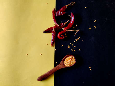 Red Chilli flakes in wooden spoon and red chillies on yellow and black background,top viewの写真素材