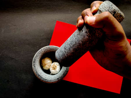 Human hand holding mortar and ready to crush the garlic in pestle. Isolated on red and black...