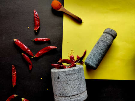 Stone made of mortar and pestle is ready to crush the red chillies. Isolated on yellow and black...