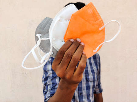 South Indian man showing three face masks in white, grey and orange color. Isolated on white background.の写真素材