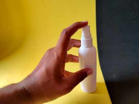Human hand hold spray bottle and ready to spray on yellow and black background
