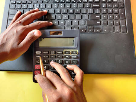 Business people using laptop and analyzing investment charts with calculator.Top view.Yellow background.の写真素材