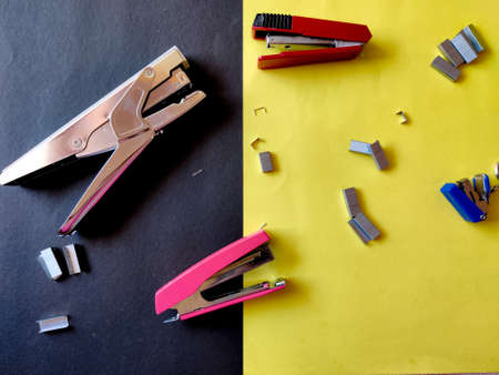 Four different sized staplers and stapler pins isolated on yellow background. Top view
