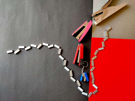 Four different sized staplers and stapler pins isolated on red,black background. Top view