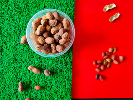 Peanuts in plastic bowl isolated on green background. And peeled nuts in red background. Selective...