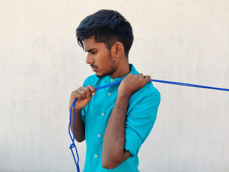 South Indian young man pulling a blue color rope behind his back.Isolated on white background.