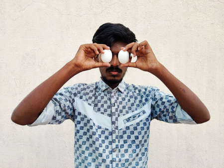 South Indian man covering his eyes with two eggsの写真素材
