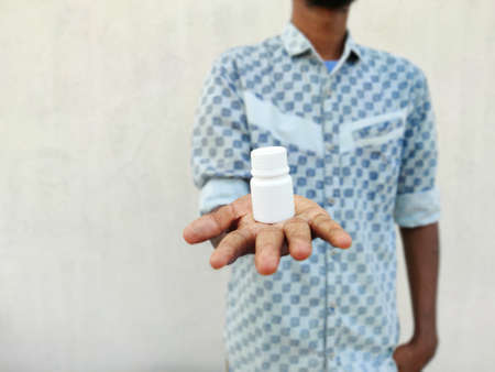 Young man with jar of pills on palm.The drug against the virus on the palm of a male hand. Isolated...