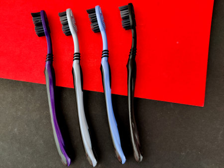 A family set of four colorful tooth brushes with black bristles. Isolated on red and black backgroundの写真素材