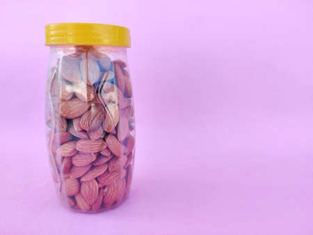 A Plastic bottle with yellow cap is filled with healthy almonds. Pink background. Copy spaceの写真素材