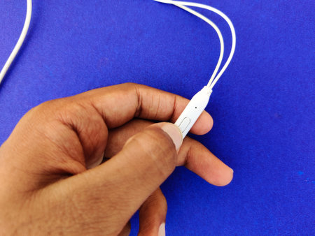 Male hand pressing the mic of white ear phone. He is trying to Pause or resume