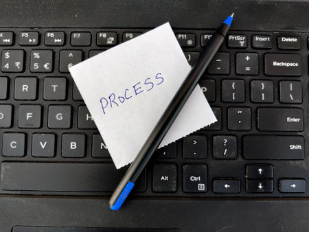 A White sticky note with text PROCESS and pen on top of laptop keyboard