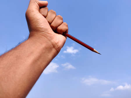 South Indian man hand holding sharp red color pencil. Isolated on cloud backgroundの写真素材