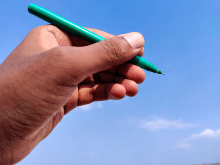 Left hand Man using green ink pen to write. Cloud background.の写真素材
