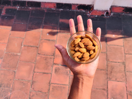 A glass bowl full of almonds on man palm.
