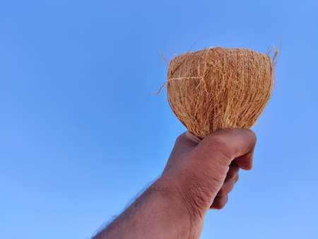 South Indian man hand holding empty coconut fruit shell. Cloud background.の写真素材