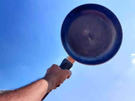 South Indian man hand holding a black color frying pan. Cloud background.