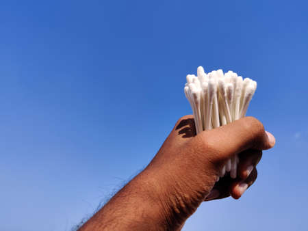 South Indian man hand holding bunch of cotton ear sticks . Cloud background.の写真素材