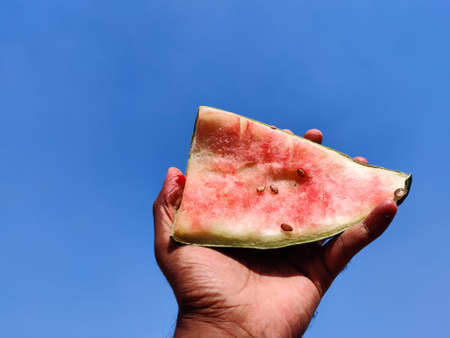 South Indian man hand holding a eaten slice of watermelon with seeds. Cloud background. Summer...
