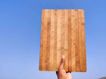 South Indian young man holding a vertical empty wooden chopping board .Cloud backgroundの写真素材