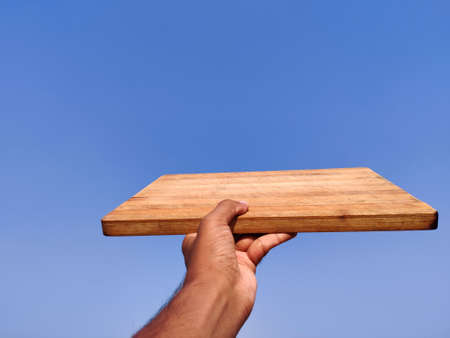 South Indian young man giving wooden chopping board .Cloud backgroundの写真素材