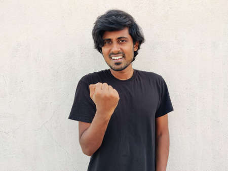 South Indian Young handsome man wearing black tshirt doing winner gesture with one arm raised and smiling. White backgroundの写真素材