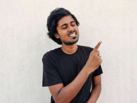Yes, Its perfect, I love that. Young smiling south Indian man in closed eyes pointing fore finger on empty space. White backgroundの写真素材