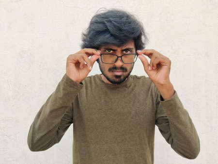 Angry south Indian young man wearing spectacles. Serious eyes. Seems he his angry of something. White background.の写真素材
