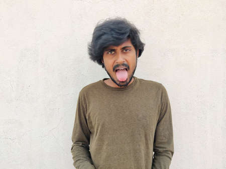 South Indian handsome man with long hairs wearing full sleeves showing his tongue. White backgroundの写真素材