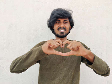 Handsome man wearing green full sleeves smiling in love doing heart symbol with hands.の写真素材