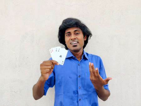 Young south Indian man holding four ace poker cards looking confident,cheerful,happy. White...