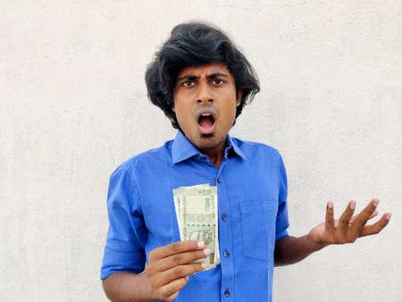 South Indian young man feeling extremely shocked and surprised holding two 500 rupees note. White backgroundの写真素材