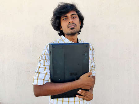 Casual looking young male student holding closed laptop in hands. Going to attend online classの写真素材