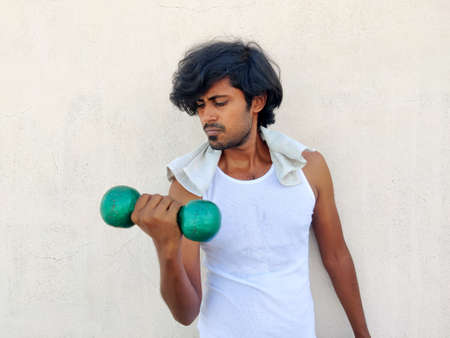 Lean Indian man in white workout clothes is doing bicep exercise with Dumbbellsの写真素材