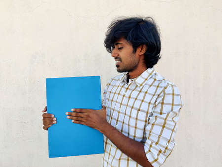 Young studying man holding a closed blue color laptop and smiling toward it. Looks he got new laptop for lockdown classes.の写真素材