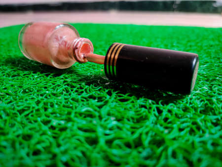 Side view of opened dripping pink color nail polish bottle. Isolated on green backgroundの写真素材