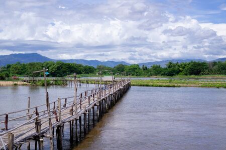 A wooden bridge over the river with a forest background Mountains and blue skiesの写真素材