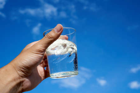 A glass of water in hand the blue sky backgroundの写真素材