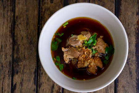 Braised pork noodles in a white bowl on a wooden tableの写真素材