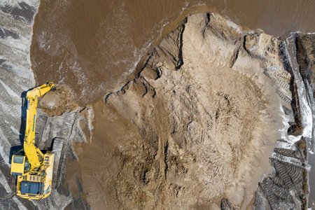 Yellow excavator digger working. Excavator digging sand, ground from water. Industrial aerial drone photo viewの写真素材