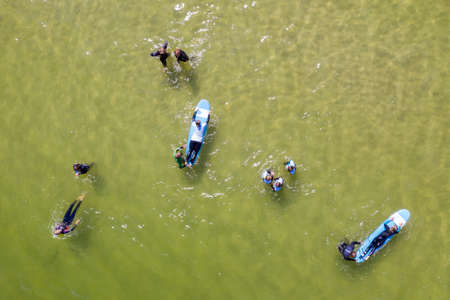 Aerial drone view of people surfing in the sea. Summer sport learning how to surf. Surfboarding in...