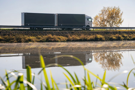 Truck goes on the road in autumn. car transportation . Truck with semi-trailer in gray color. Transport truck drives in autumn by the lake in sunny day.の写真素材