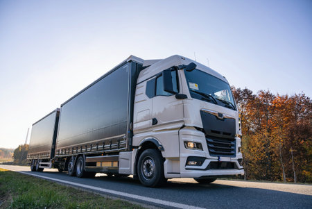 Truck is driving through the forest in autumn. Truck with semi-trailer in gray color. transportation