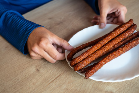 The woman holds food in her hand. The girl holds kabanos sausages on a plate. Holding sausages in hand.の写真素材