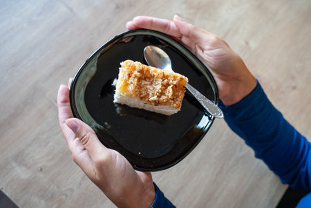 The woman holds food in her hand. The girl holds a cake on a plate. Cake on black plate.