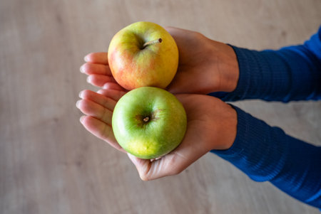 The woman holds food in her hand. The girl holds an apple. Apples in woman's hands. Two green apples