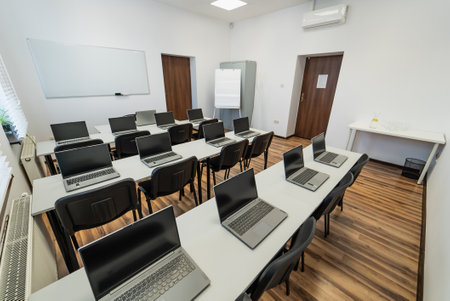 Interior of a modern classroom with desks, chairs and laptops. Empty conference room with laptop on table in office. OfficeBusiness. Conference room with benches, tables and a laptops on the tables.の写真素材