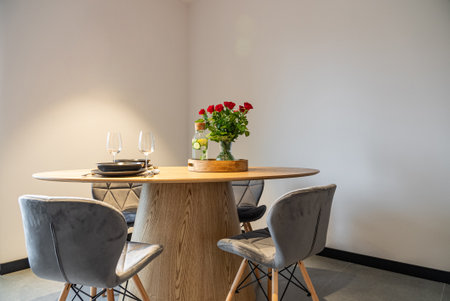 Dining table with plates, glasses and vase of red roses. Interior of a Modern furnished Kitchen in a...