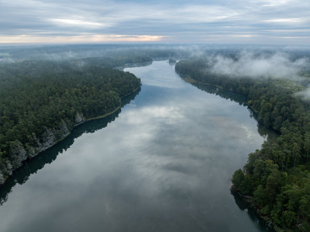 Aerial drone view of a lake surrounded by green forest. Big lake in the fog and clouds. Kulka Reserve, Masuria, Poland. Lake in the Masurian Lake District. Lake Lesk in the Kulka Reserve in Poland.の写真素材