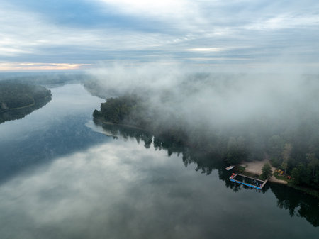 Aerial drone view of a lake surrounded by green forest. Big lake in the fog and clouds. Kulka Reserve, Masuria, Poland. Lake in the Masurian Lake District. Lake Lesk in the Kulka Reserve in Poland.の写真素材